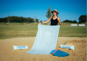 Frau breitet graues Strandtuch 190 x 90 cm mit aufblasbarem Kopfkissen am Strand aus