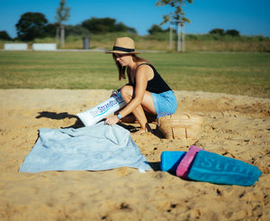 Frau steckt aufblasbares Kopfkissen in graues Strandtuch 190 x 90 cm am Strand