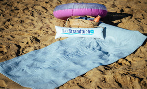 Graues Strandtuch 190 x 90 cm mit aufblasbarem Kopfkissen aus 100 % Baumwolle am Strand ausgebreitet aus dem Onlineshop DasStrandtuch.com