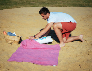 Mann steckt aufblasbares Kopfkissen in rosa Strandtuch 150 x 90 cm aus 100% Baumwolle aus dem Onlineshop DasStrandtuch.com