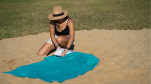 Frau steckt aufblasbares Kopfkissen in grünes Strandtuch 150 x 90 cm aus 100% Baumwolle am Strand