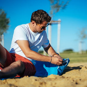 Mann verstaut Smartphone in der eingenähten Tasche des blauem Strandtuchs 190 x 90 cm aus 100% Baumwolle